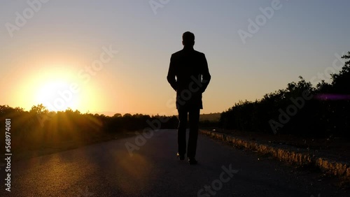 Silhouette of a man is walking on a road at golden sunset.