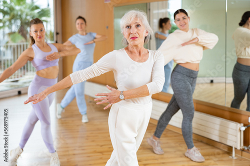 Senior female choreographer showing new dancing dynamic movements during training together with women in studio