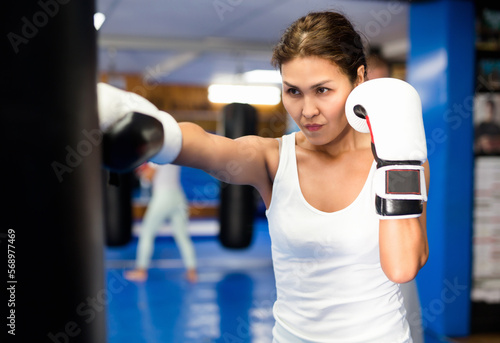Asian woman in boxing gloves exercising jabs with punchbag during her boxing training. © JackF
