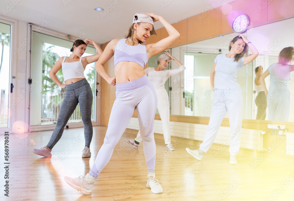 Fototapeta premium Practiced middle-aged woman engaging in fitness dance in dance studio during workout session. Women training dance in hall