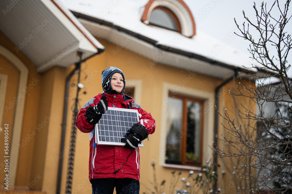 Obraz premium Boy with solar panel against house in winter. Alternative energy concept.