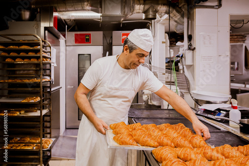 Male baker checking croissant on tray photo