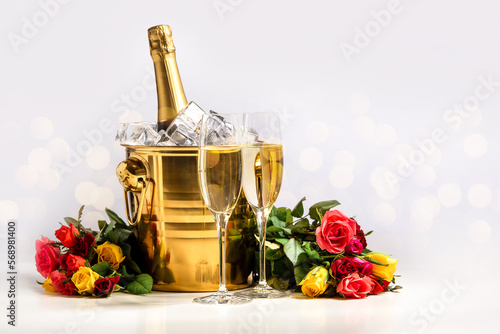 Obraz na płótnie Two glasses of champagne, a bucket with a bottle of champagne and ice and a bouquet of multi-colored roses on a white background w salonie