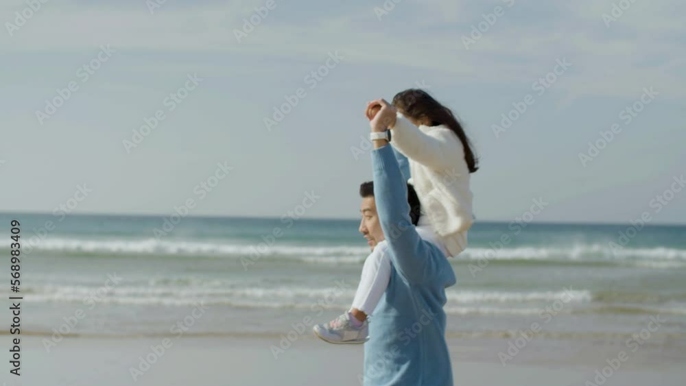 Happy father and cute little daughter having fun at seashore. Asian dad carrying adorable long-haired girl on his shoulders while singing and having great time. Family, fun, childhood concept