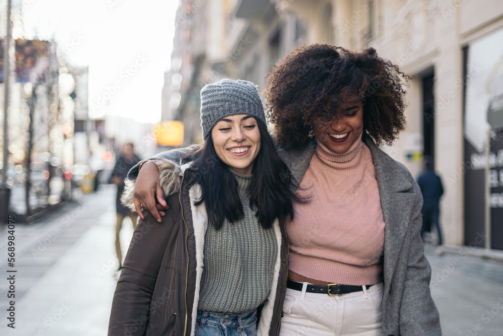 Female friends walking embraced through the city in winter Female friends walking embraced through the city in winter