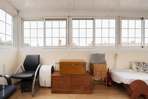 A room full of unconnected junk with trunks and a bed under a bay window with French-style white aluminum windows photo