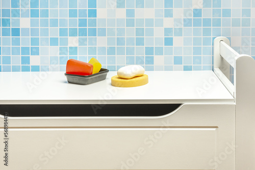 Black porcelain bowl with bars of glycerin soap, a white bar of soap on a yellow sponge and all on a white cabinet photo