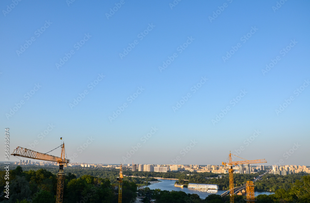 Obraz premium Tower crane on the background of Dnipro river and left bank of Kyiv city. New buildings architecture and industry construction
