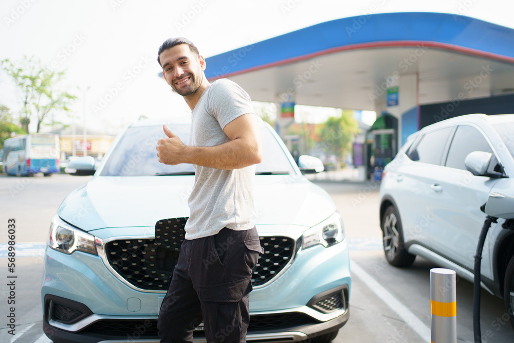Handsome Asian young man holding an EV plug connector and attaching onto the car, man plugged in the EV charging connector to the vehicle. Handsome Asian young man holding an EV plug connector and attaching onto the car, man plugged in the EV charging connector to the vehicle.
