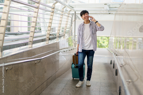 Asian young man dragging a suitcase along the city or airport terminal with shopping bags.