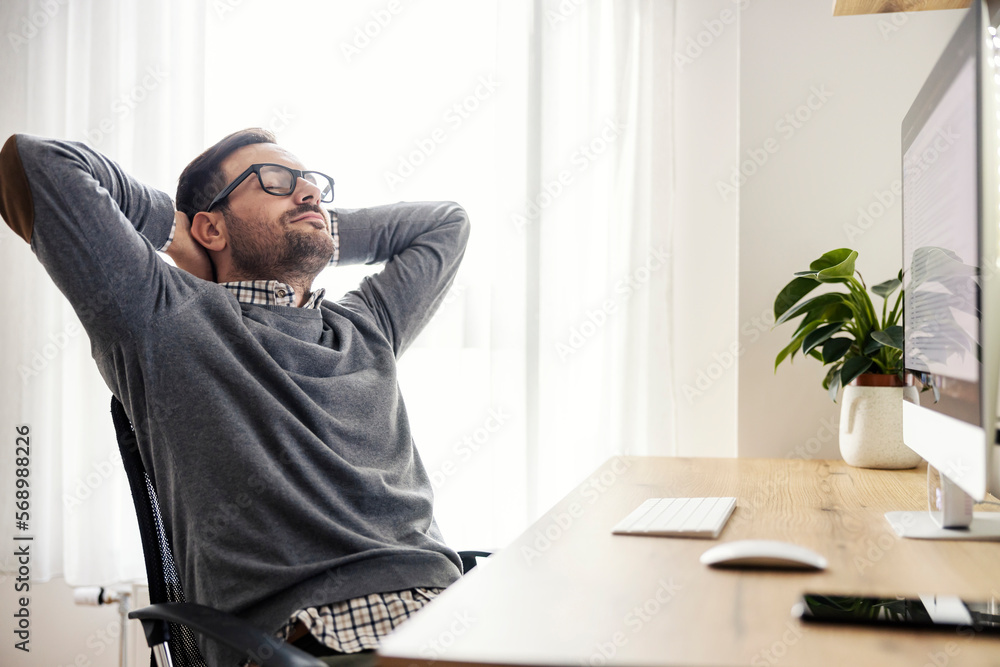 A relaxed freelancer sits in his chair and has work break at home office. - obrazy, fototapety, plakaty 