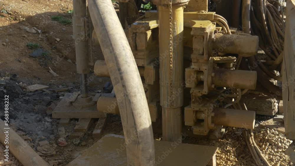 CLOSE UP: Heavy industrial rig bores a hole in the ground during modern geothermal pump installation. Massive drill spins and drills into the soil at a construction site in the sunny countryside. CLOSE UP: Heavy industrial rig bores a hole in the ground during modern geothermal pump installation. Massive drill spins and drills into the soil at a construction site in the sunny countryside.