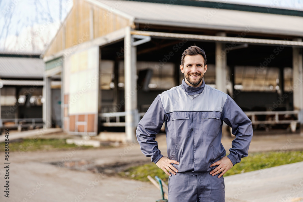 A confident farmer is standing in outdoors in front of barns and smiling at the camera. A confident farmer is standing in outdoors in front of barns and smiling at the camera.