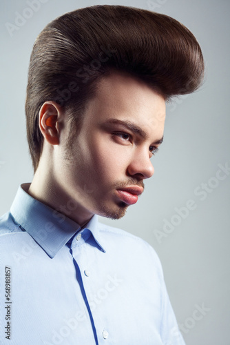 Side view portrait of handsome confident man with mustache and beard with retro classic elvis presley hairstyle, looking away, wearing blue shirt. Indoor studio shot isolated on gray background.