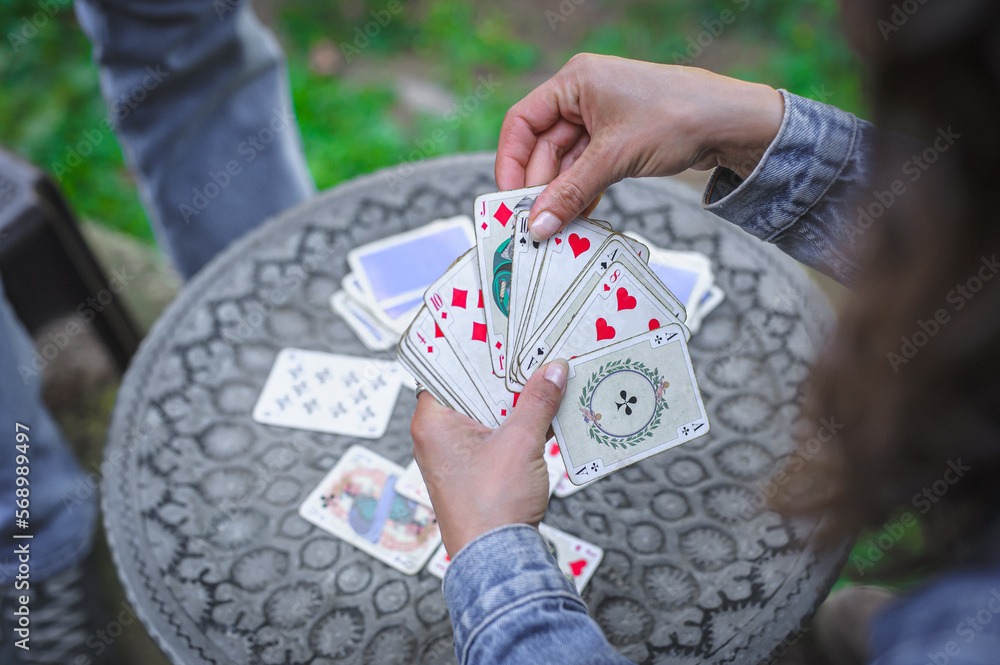Obraz premium Card playing in a spring garden: Couple are sitting on a table, relaxing and playing cards together. Blurry background.