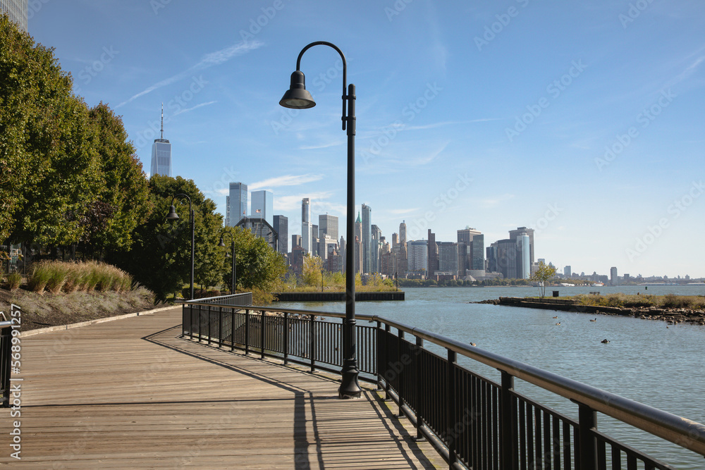 walkway on embankment of Hudson river with scenic view of skyscrapers of New York City.