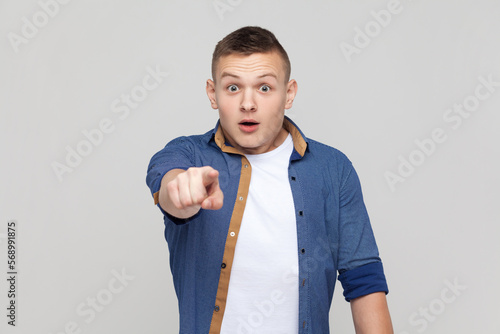Portrait of astonished amazed handsome teenager boy wearing blue shirt pointi...