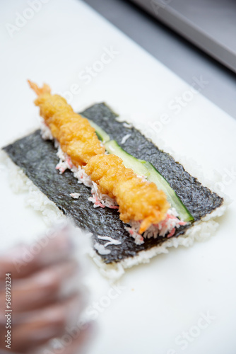 A view of the process of making a sushi roll, featuring tempura shrimp.