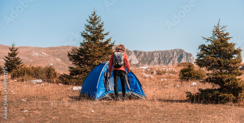 A man with a tent enjoys a sunny day whileusing a smartphone and camping in the mountains