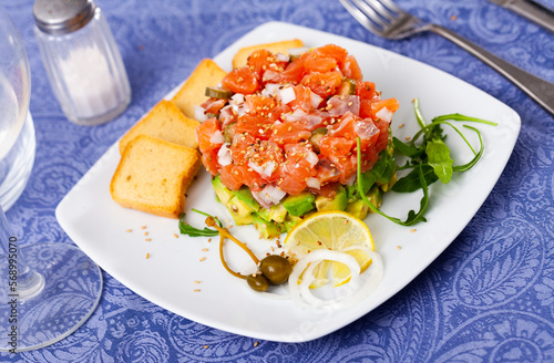 Raw salmon tartare with avocado and sesame seeds served with toasted bread and lemon
