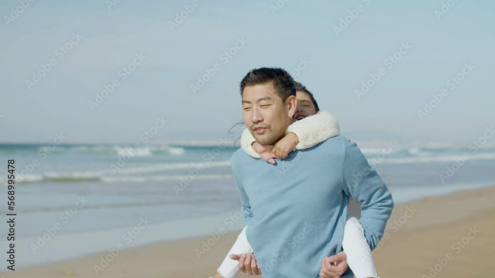 Asian father and little daughter strolling along seashore on sunny day together. Dad telling stories and carrying child on his back while kid having fun. Parenthood, family, happiness concept Asian father and little daughter strolling along seashore on sunny day together. Dad telling stories and carrying child on his back while kid having fun. Parenthood, family, happiness concept