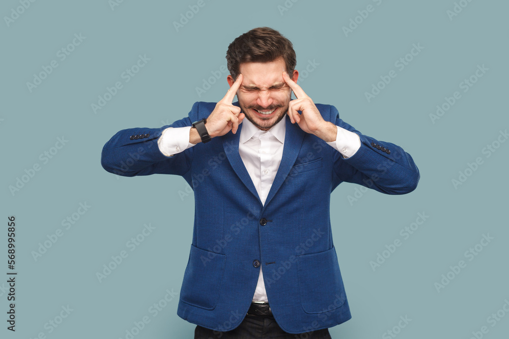 Sick ill frustrated man with mustache standing with hands on hand, frowning face from pain, suffering headache, wearing white shirt and jacket. Indoor studio shot isolated on light blue background. Sick ill frustrated man with mustache standing with hands on hand, frowning face from pain, suffering headache, wearing white shirt and jacket. Indoor studio shot isolated on light blue background.