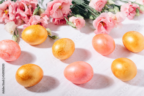 Gold and pink painted Easter eggs in pastel colors and flower bouquet on a white cotton tablecloth