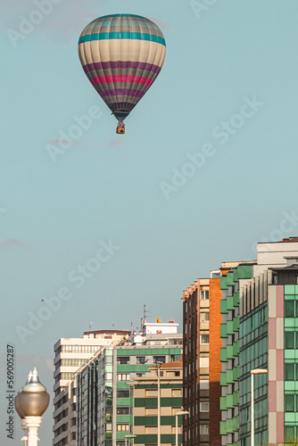 A vertical photo of a colorful hot air balloon flying around a free blue sky with Asturias buildings below it