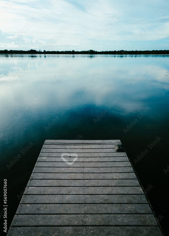 wooden pier with heart engraving on lake reflecting clouds