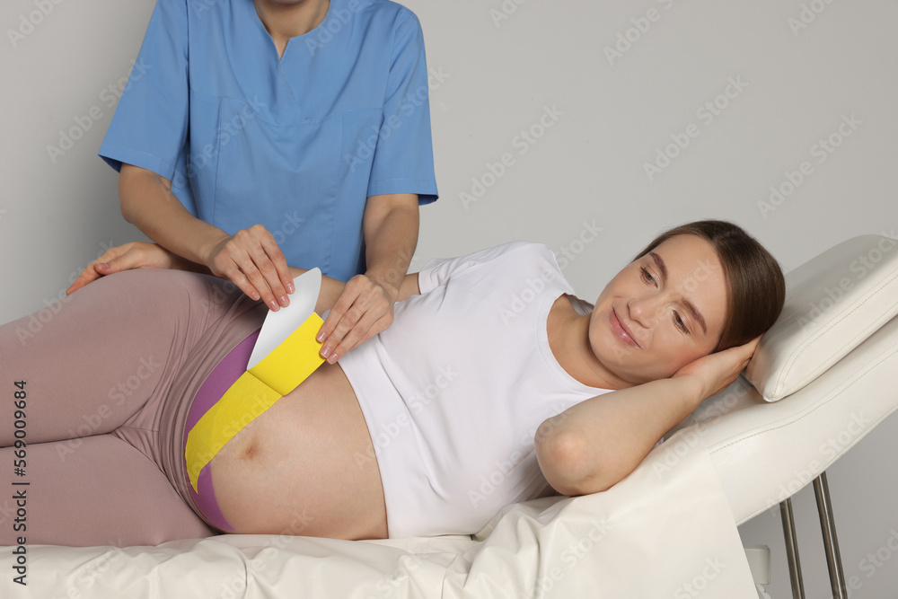 Pregnant woman visiting physiotherapist. Doctor applying kinesio tape indoors, closeup Pregnant woman visiting physiotherapist. Doctor applying kinesio tape indoors, closeup
