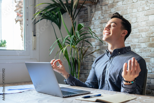 Serene office male employee sit at desk relaxing doing yoga, practice meditation to reduce stress relief fatigue feel internal balance at workplace, improve mindfulness, maintain mental health concept photo