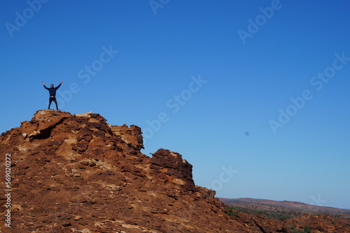 Man conquers mountain top, desert mountain man throws up arms in celebration, having reached the ultimate goal