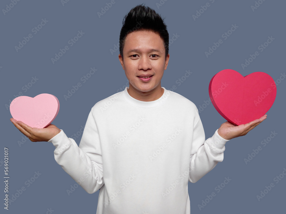 Handsome man holding small heart shape and big heart shape while smiling Handsome man holding small heart shape and big heart shape while smiling
