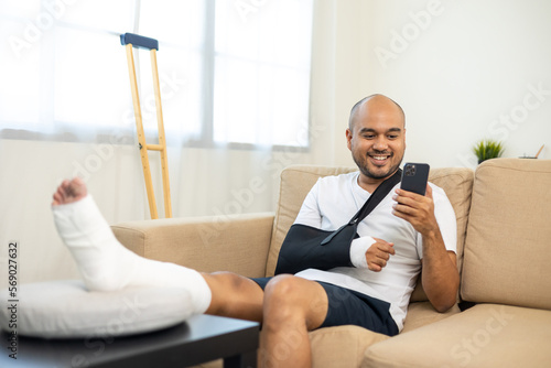 Man recovery from accident fracture broken bone injury with leg splints in cast neck splints collar arm splints sling support arm using smartphone. Social security and health insurance concept.