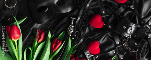 Explore the world of kinky play. Top view of bdsm leather kit against of a black silk. tulips. Horizontal wide photo subtitle, cover. copy-space