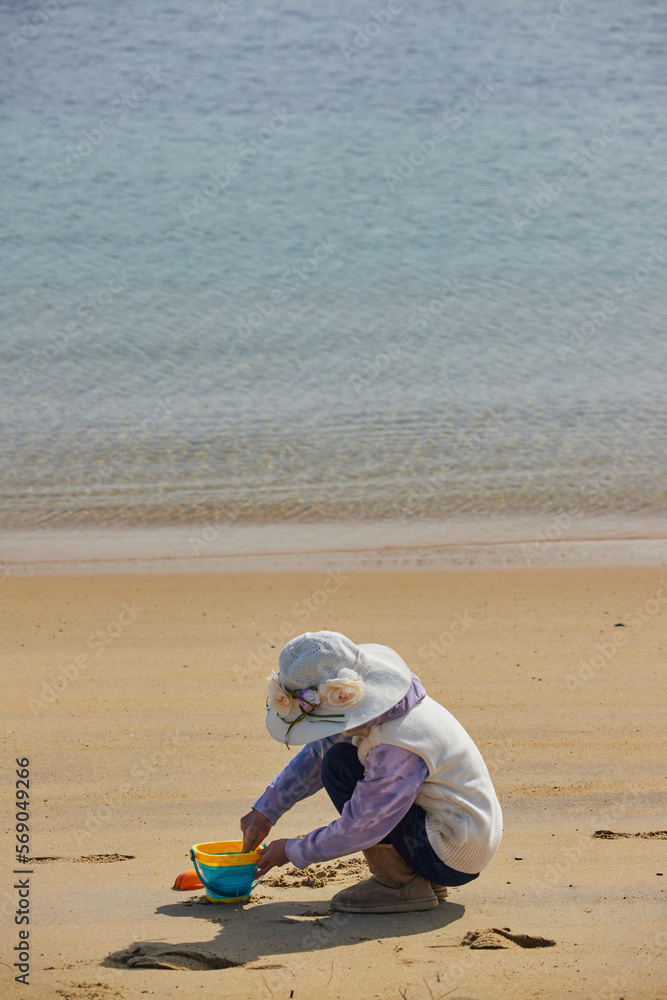 Obraz premium 冬の海岸のビーチで砂遊びしている小学生の女の子の様子