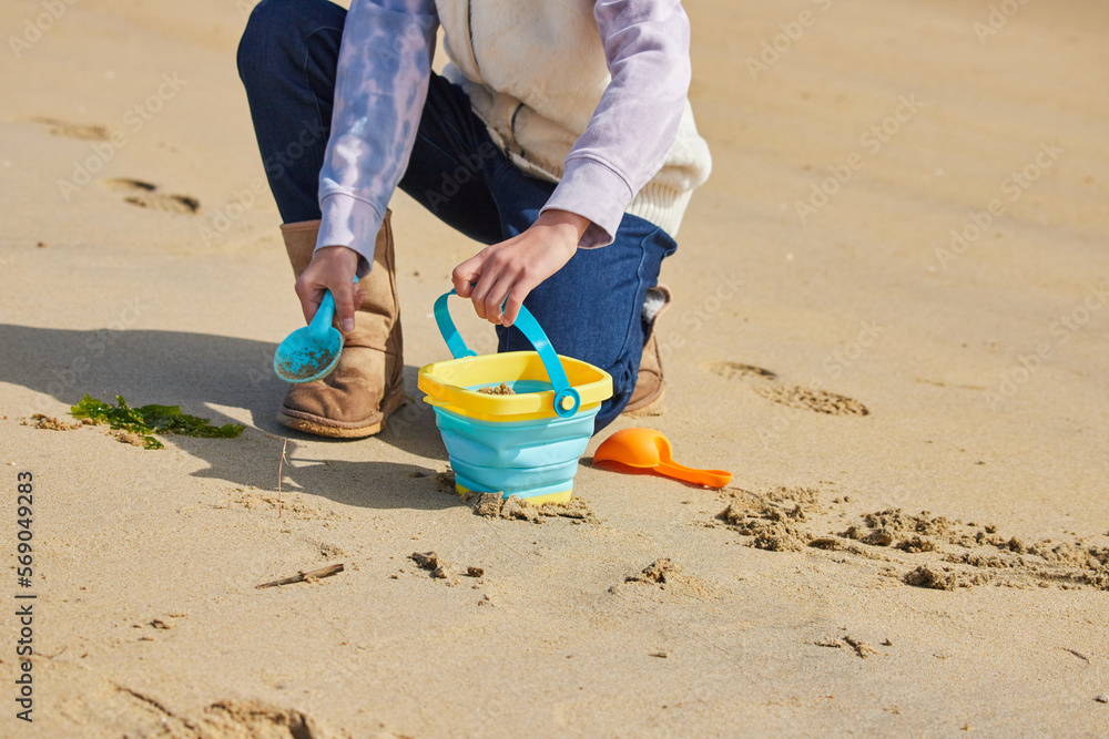 冬の海岸のビーチで砂遊びしている小学生の女の子の様子