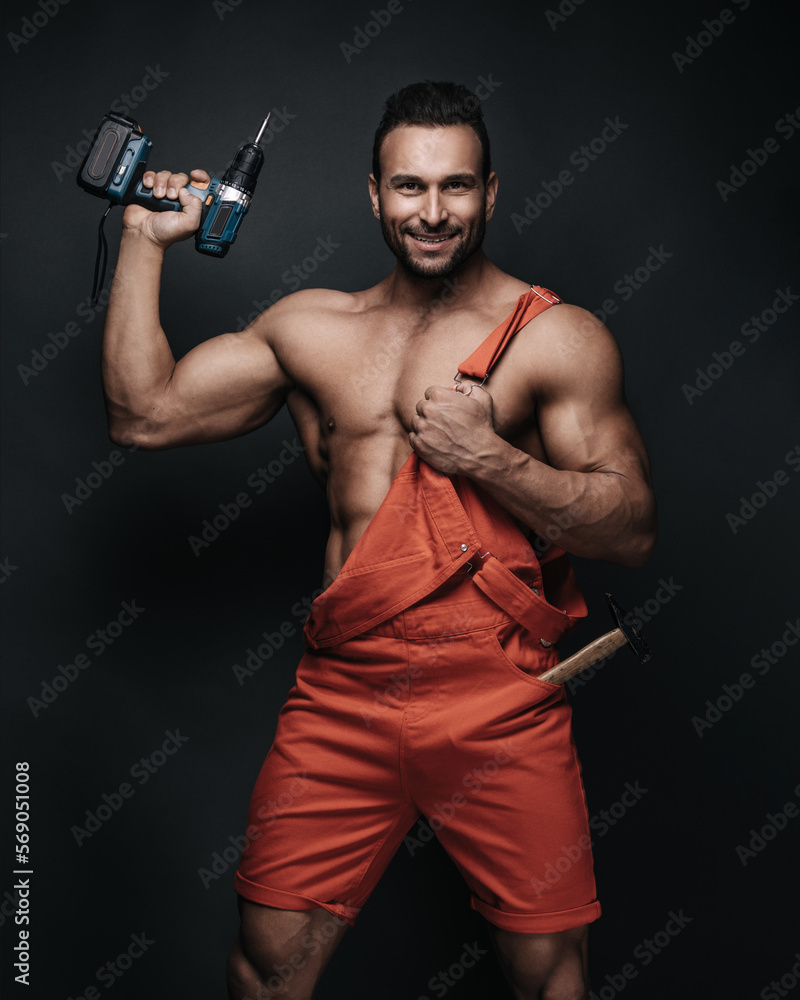 Handsome man in red jumpsuit on dark background in studio. Sexy handyman with tools. Male worker portrait with screwdriver. Handsome man in red jumpsuit on dark background in studio. Sexy handyman with tools. Male worker portrait with screwdriver.