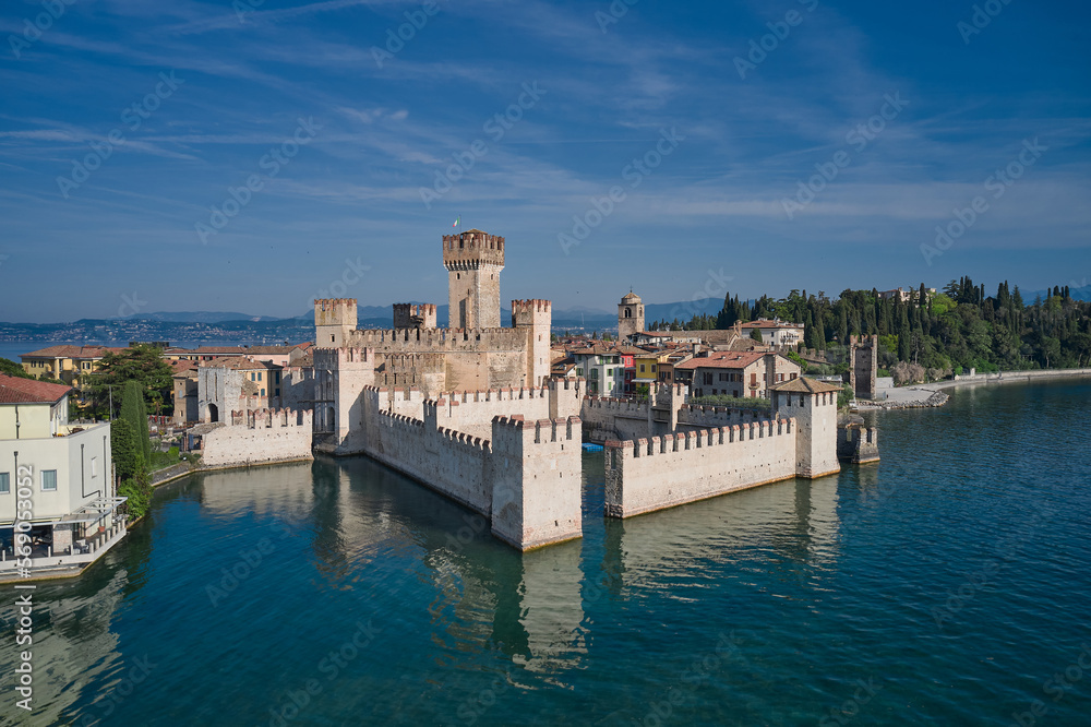 Scaligero Castle drone view. Italian castles Scaligero on the water. Sirmione top view. Flag of Italy on the towers of the castle on Lake Garda. Popular travel destination on Lake Garda in Italy.