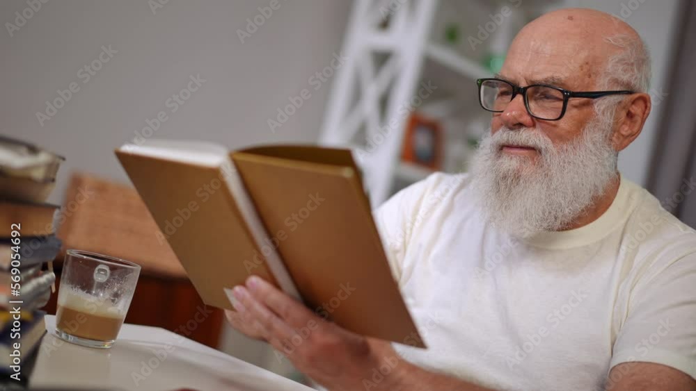 Angle view portrait of intelligent confident senior man in eyeglasses reading turning book page. Concentrated absorbed Caucasian retiree enjoying hobby at home. Leisure and lifestyle concept Angle view portrait of intelligent confident senior man in eyeglasses reading turning book page. Concentrated absorbed Caucasian retiree enjoying hobby at home. Leisure and lifestyle concept
