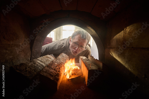 Homeowner makes fire in firebox of wood burning stove to heat home.