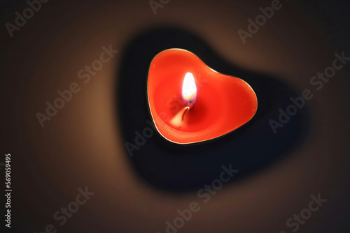Candle in the shape of a heart burns in the dark