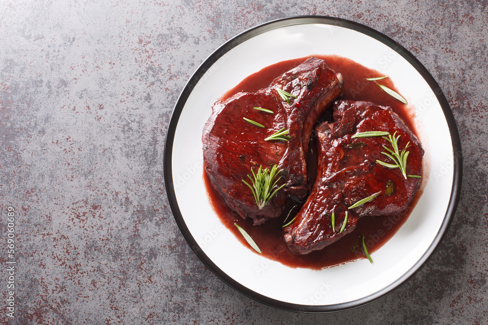Maiale ubriaco is a traditional Tuscan dish simmered pork chops with red wine closeup on the plate on the table. Horizontal top view from above Maiale ubriaco is a traditional Tuscan dish simmered pork chops with red wine closeup on the plate on the table. Horizontal top view from above