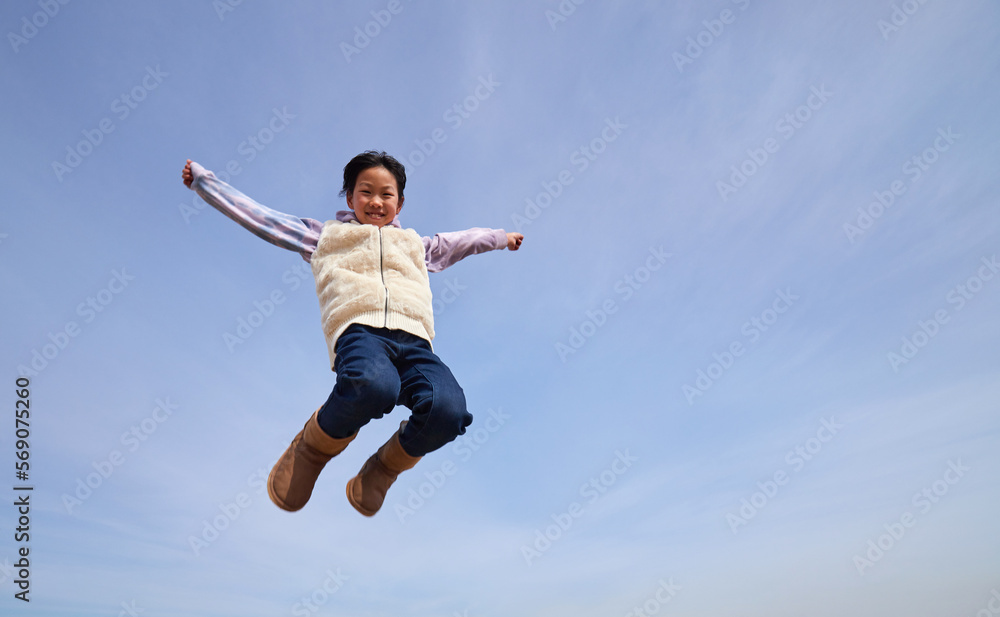 冬の青空と元気で空にジャンプしている小学生の女の子の様子