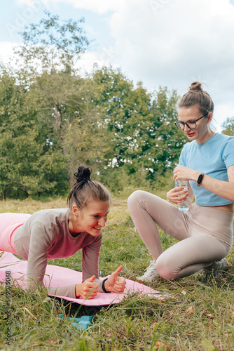 Two millennial women working out outdoor together in park. smiling happy Female holding plank position. Friends doing abs exercises enjoying physical training. Girl count use smart watch on your hand