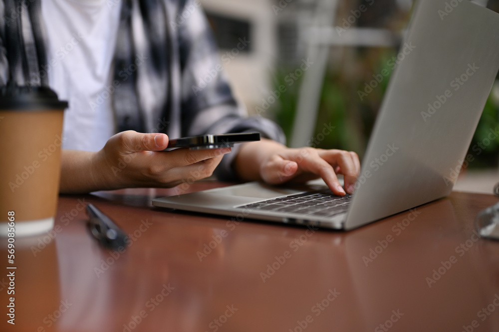 Cropped image of a female remote working at the cafe, using her smartphone and laptop Cropped image of a female remote working at the cafe, using her smartphone and laptop