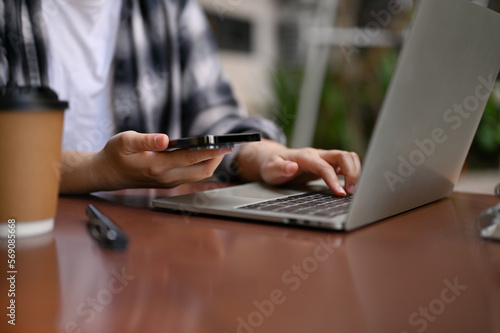 Cropped image of a female remote working at the cafe, using her smartphone and laptop