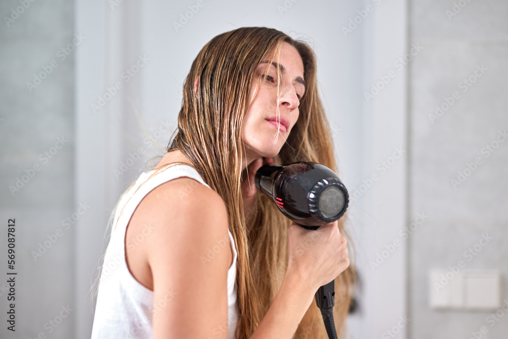 Woman drying wet hair. Side view of female with hair dryer blowing hot