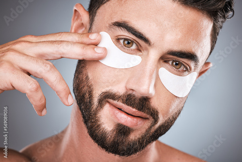 Face, skincare and man with eye patches in studio isolated on a gray background for wellness. Portrait, dermatology and male model with cosmetics, facial treatment or mask product for healthy skin.