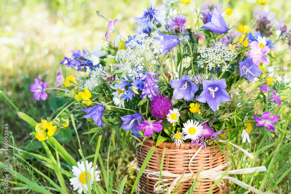 Meadow flowers bouquet in wicker mug on nature background outdoors in natural morning light, still life with vivid wild flowers in background of nature in summertime, close up view